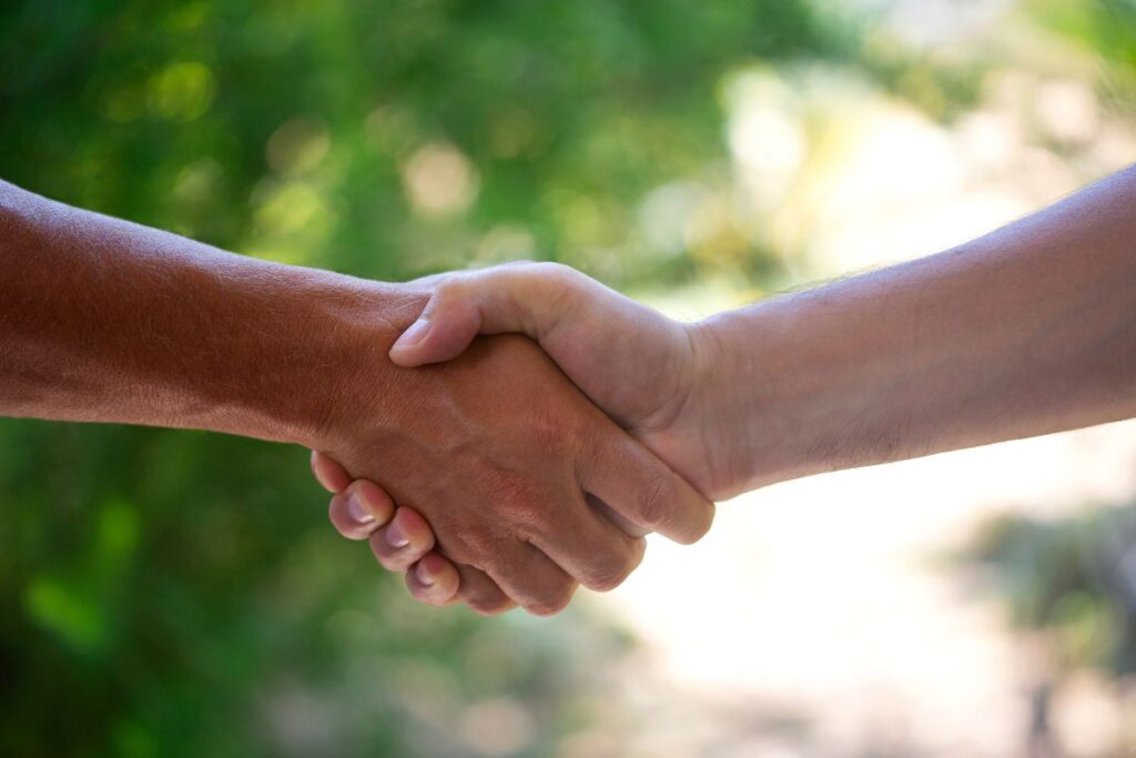 A close up of a property manager and an arborist shaking hands in front of trees